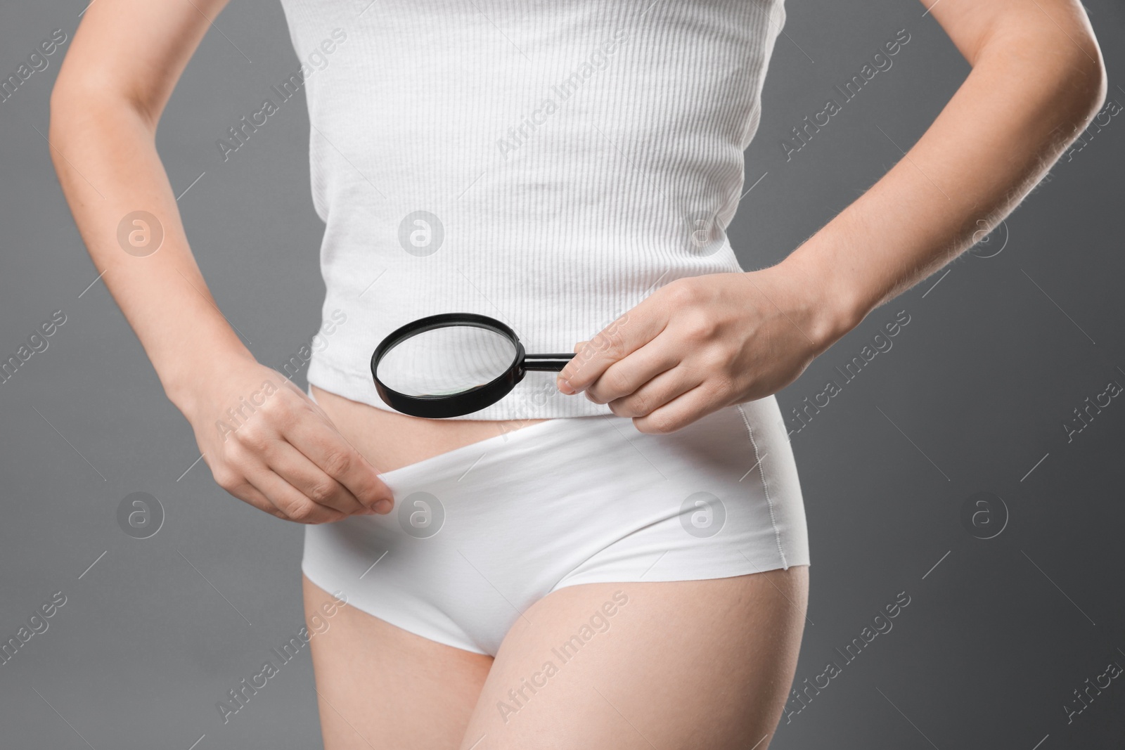 Photo of STD (sexually transmitted disease). Woman examining genital area with magnifying glass on grey background, closeup