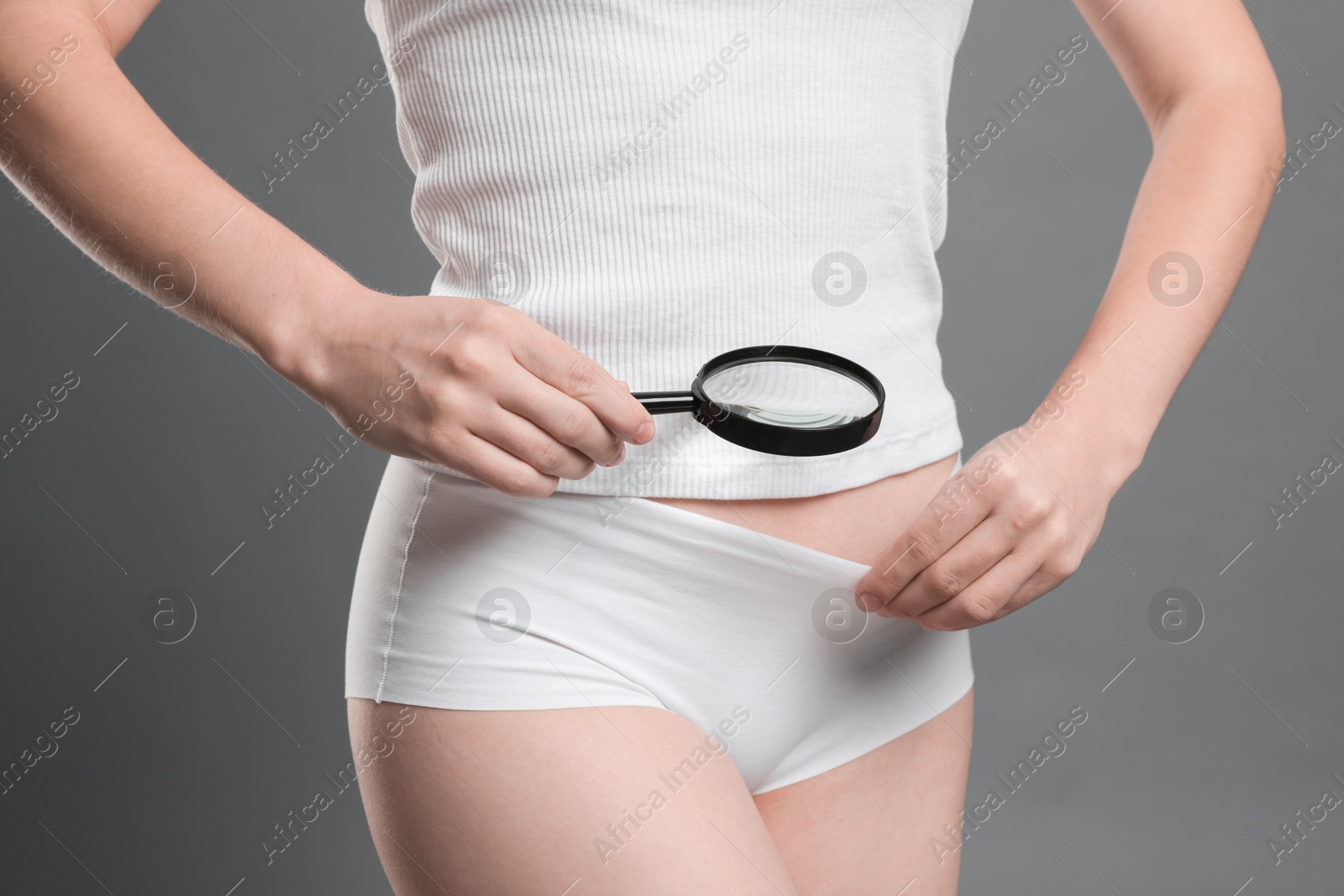 Photo of STD (sexually transmitted disease). Woman examining genital area with magnifying glass on grey background, closeup