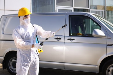 Pest control worker with spray tank near gray minibus outdoors