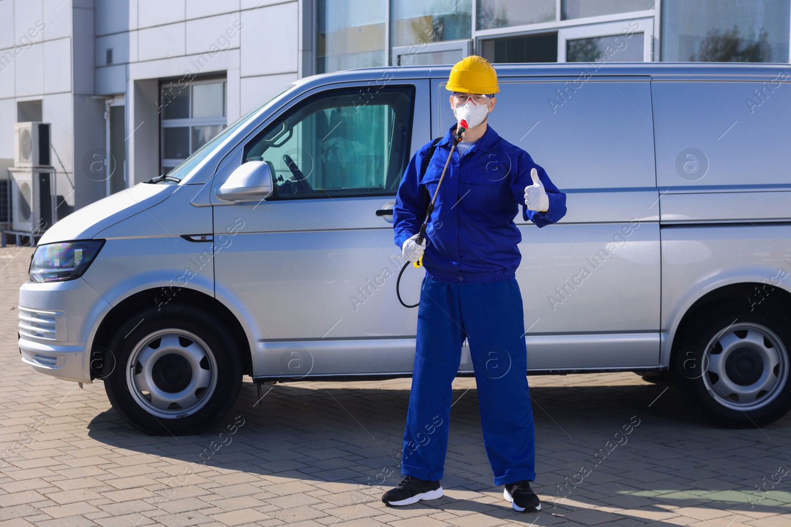 Photo of Pest control worker with spray tank showing thumbs up outdoors