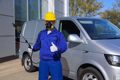 Photo of Pest control worker with spray tank showing thumbs up outdoors