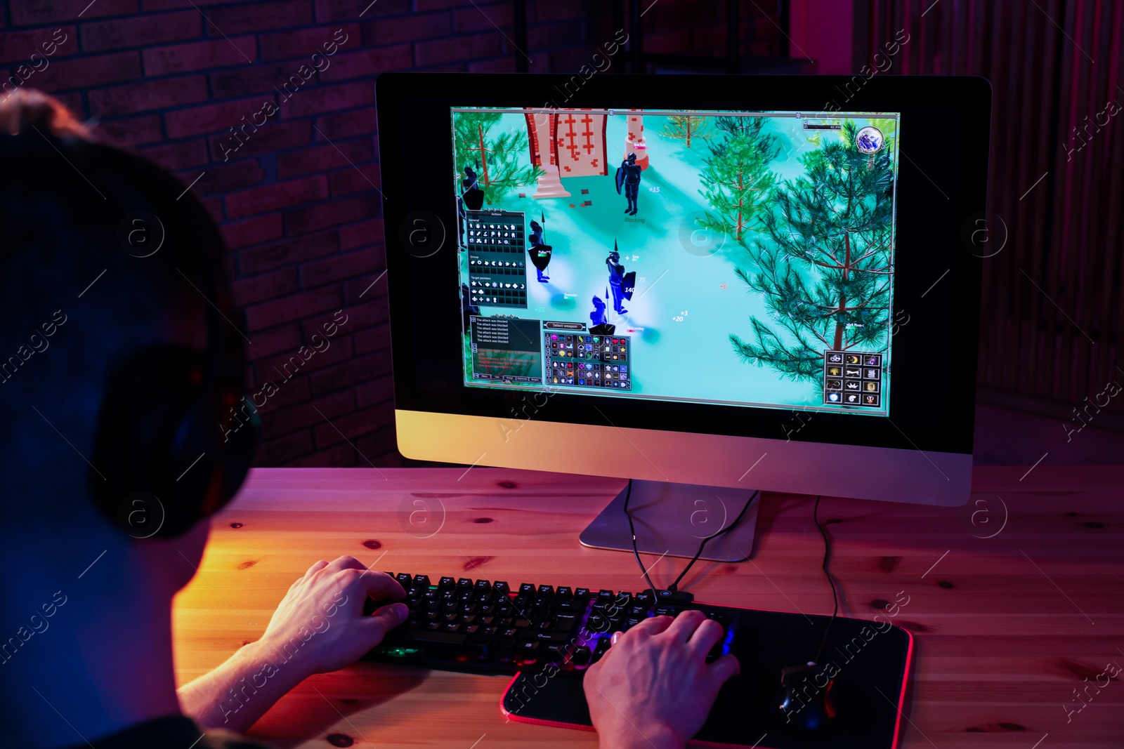 Photo of Young man playing video game with keyboard at wooden table indoors, back view