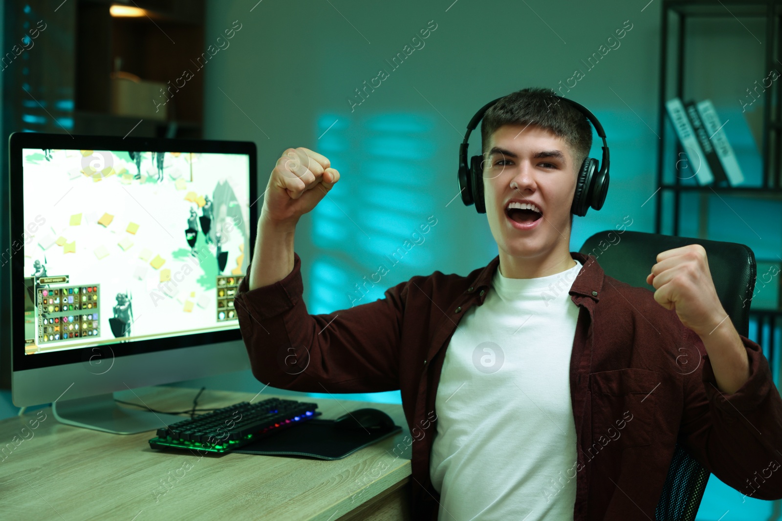 Photo of Young man playing video game with keyboard at wooden table indoors