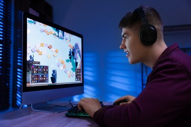 Photo of Young man playing video game with keyboard at wooden table indoors