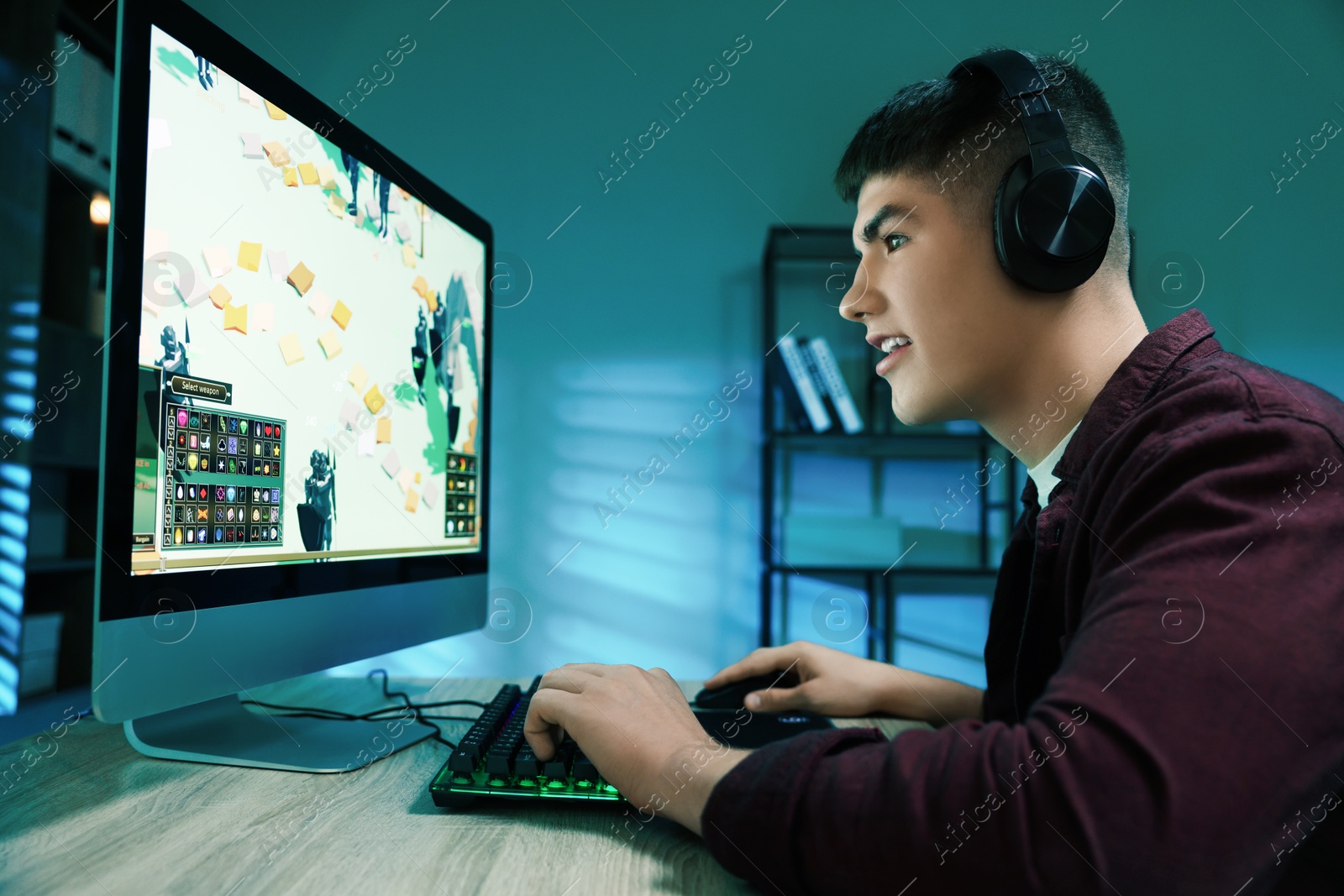 Photo of Young man playing video game with keyboard at wooden table indoors