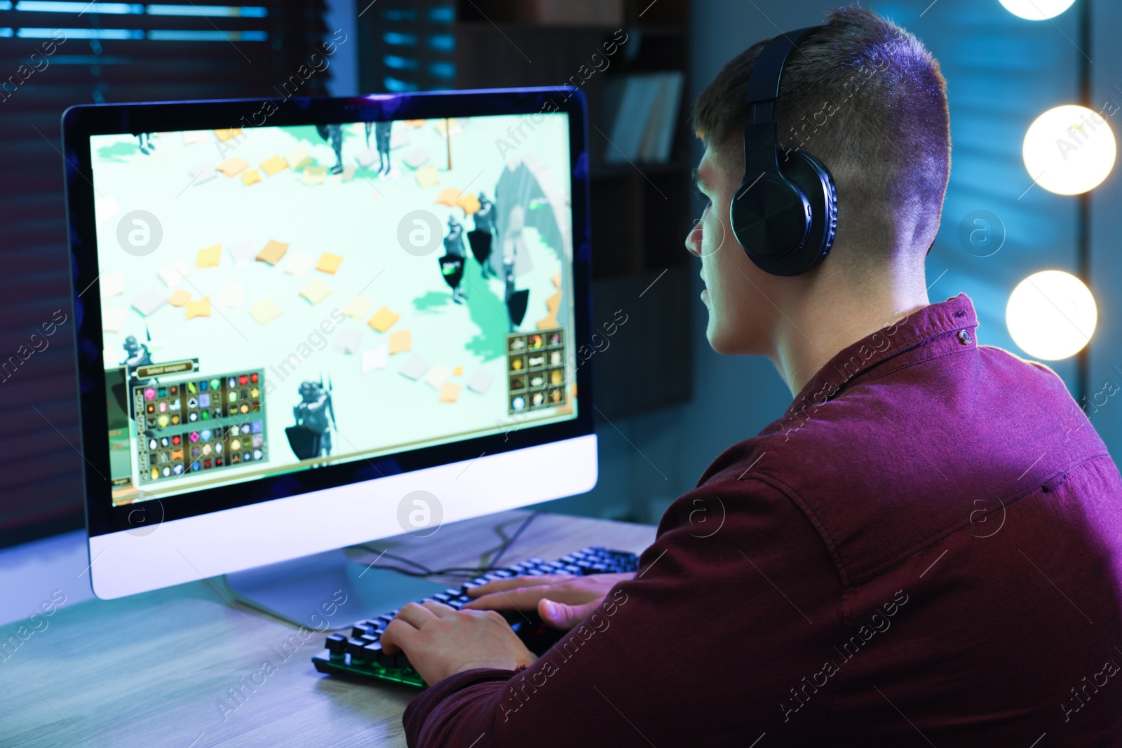 Photo of Young man playing video game at wooden table indoors, back view