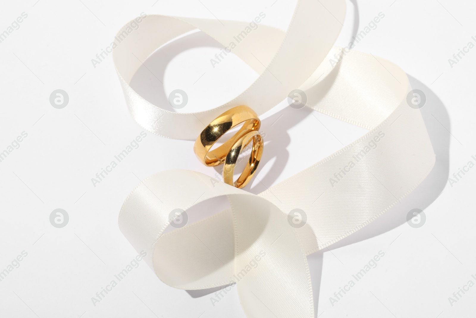 Photo of Golden wedding rings and ribbon on white background, closeup