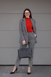 Photo of Beautiful woman in stylish suit near grey wall outdoors