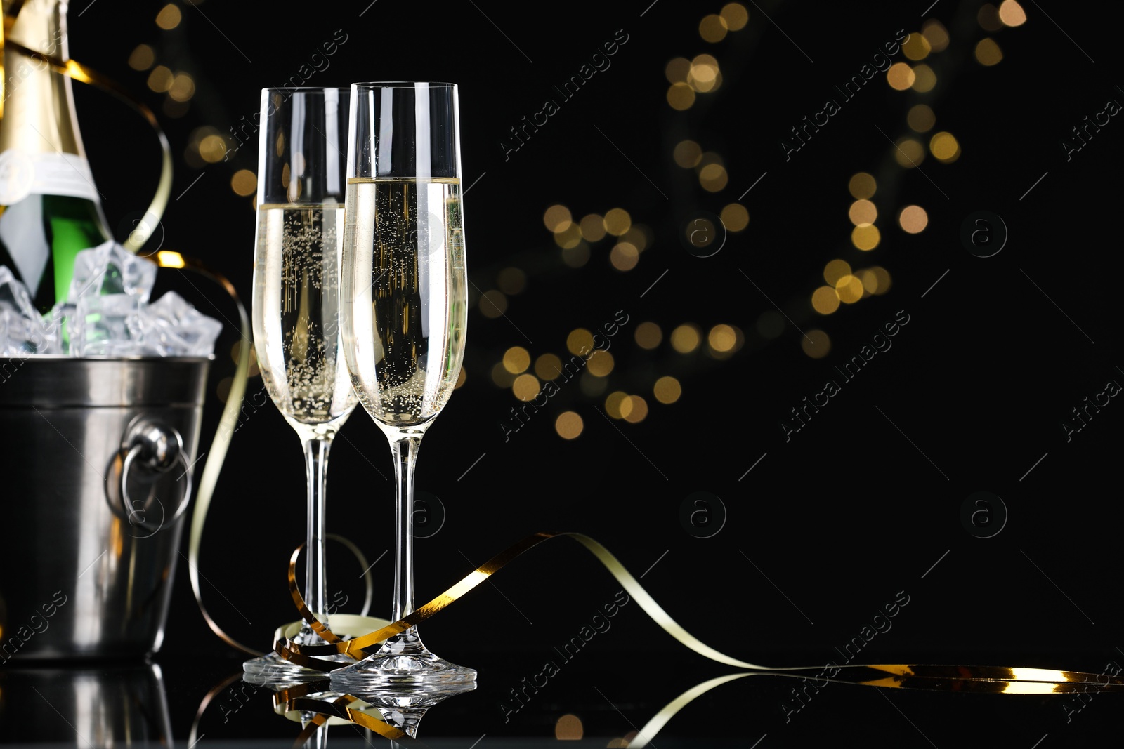 Photo of Champagne and bucket of ice on mirror surface against black background with blurred lights, space for text