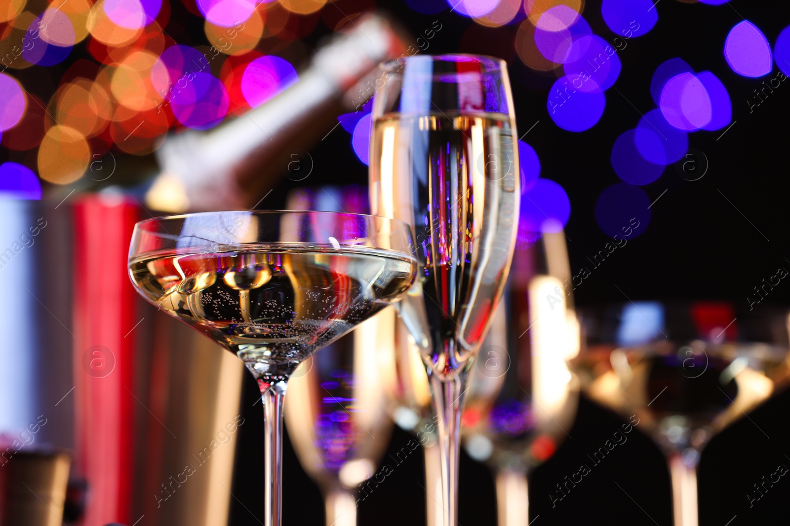 Photo of Champagne in glasses against black background with blurred lights, closeup