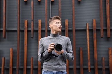 Professional photographer with modern camera near wall outdoors