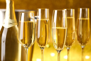 Photo of Champagne in glasses, bottle and ice bucket on golden background, closeup