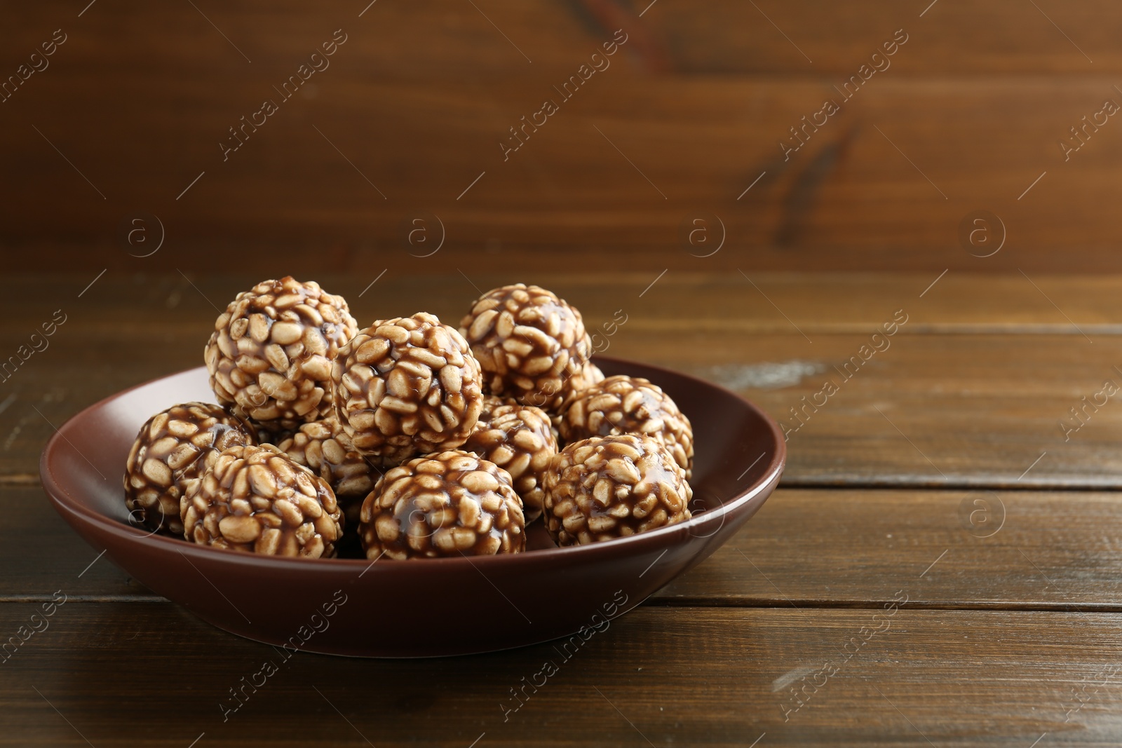 Photo of Delicious chocolate puffed rice balls in bowl on wooden table. Space for text