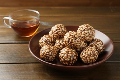 Photo of Delicious chocolate puffed rice balls in bowl and tea on wooden table, closeup