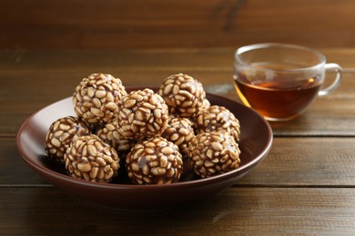 Photo of Delicious chocolate puffed rice balls in bowl and tea on wooden table, closeup