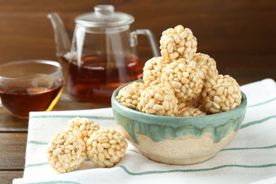 Delicious puffed rice balls in bowl and tea on wooden table, closeup