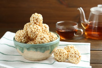 Photo of Delicious puffed rice balls in bowl and tea on wooden table, closeup