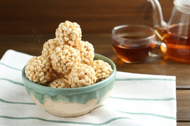 Photo of Delicious puffed rice balls in bowl and tea on wooden table, closeup