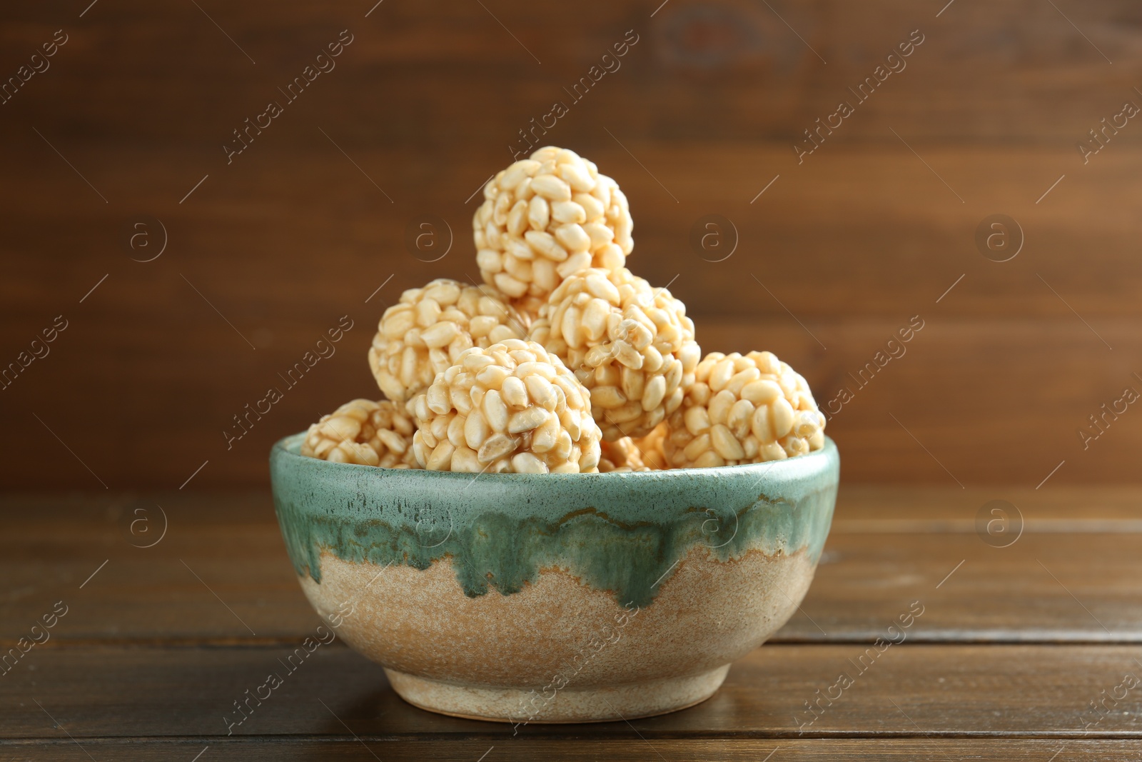 Photo of Delicious puffed rice balls in bowl on wooden table, closeup