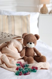 Photo of Laundry detergent capsules, teddy bear and basket with clean linens on bed indoors