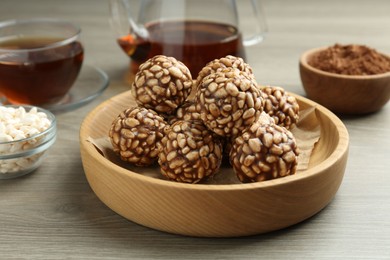 Photo of Tasty chocolate puffed rice balls served with tea on wooden table, closeup