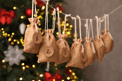 Photo of Advent calendar with gifts hanging near Christmas tree indoors