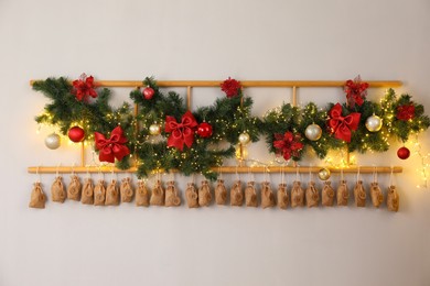 Photo of Christmas advent calendar with gifts and decor hanging on white wall indoors