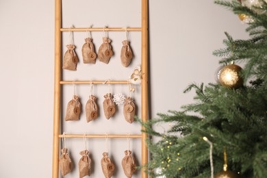 Photo of Advent calendar with gifts hanging on white wall near Christmas tree indoors