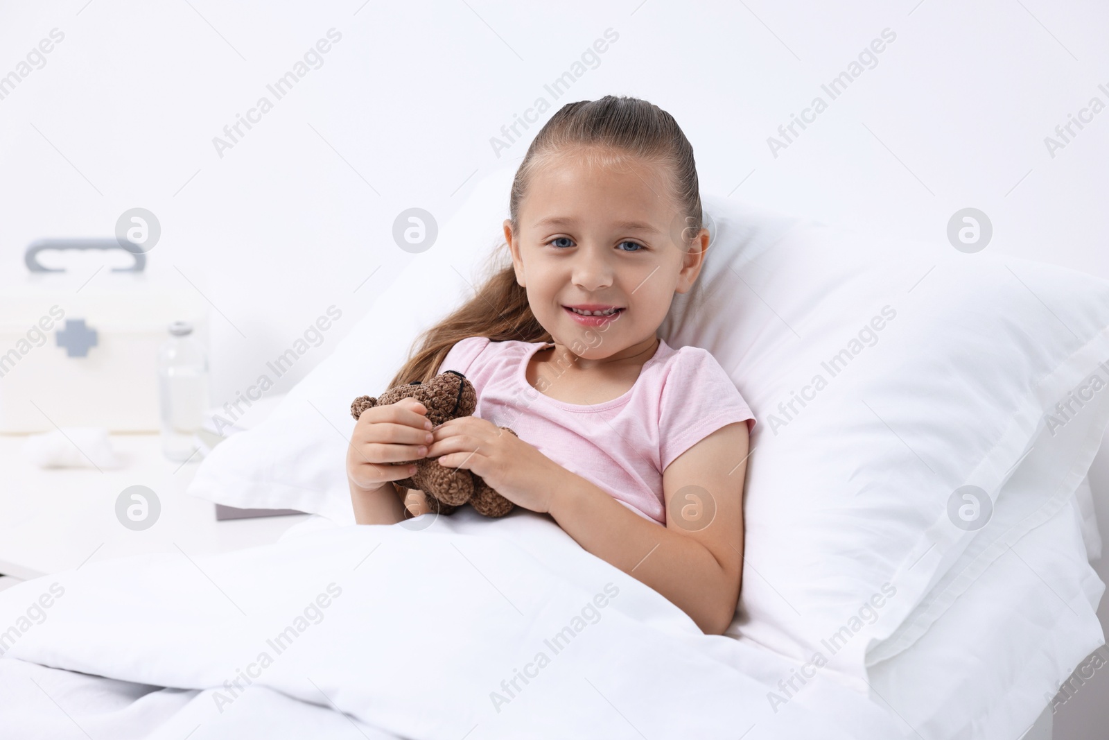 Photo of Cute little girl with teddy bear on bed in hospital