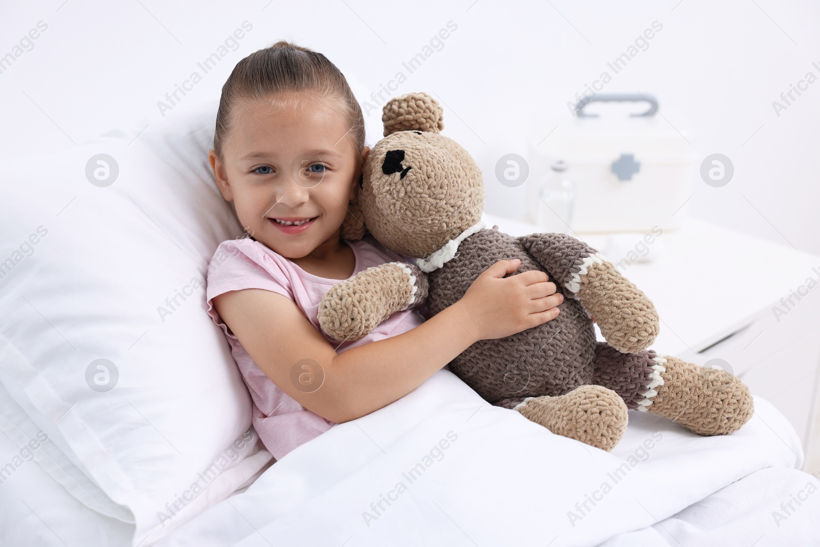 Photo of Cute little girl with teddy bear on bed in hospital