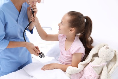 Photo of Doctor examining little girl on bed at hospital, closeup