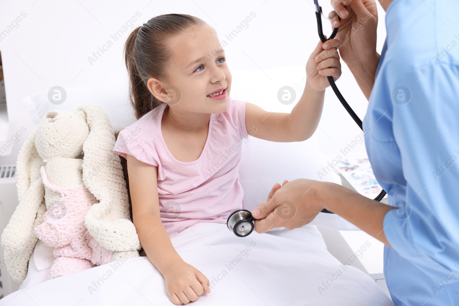 Photo of Doctor examining little girl on bed at hospital, closeup