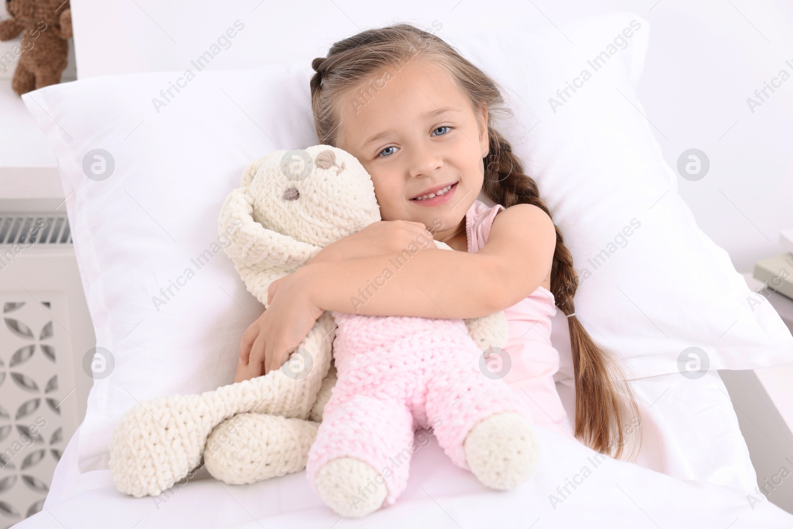 Photo of Cute little girl with toy bunny on bed in hospital