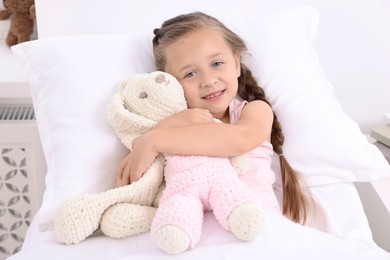 Photo of Cute little girl with toy bunny on bed in hospital