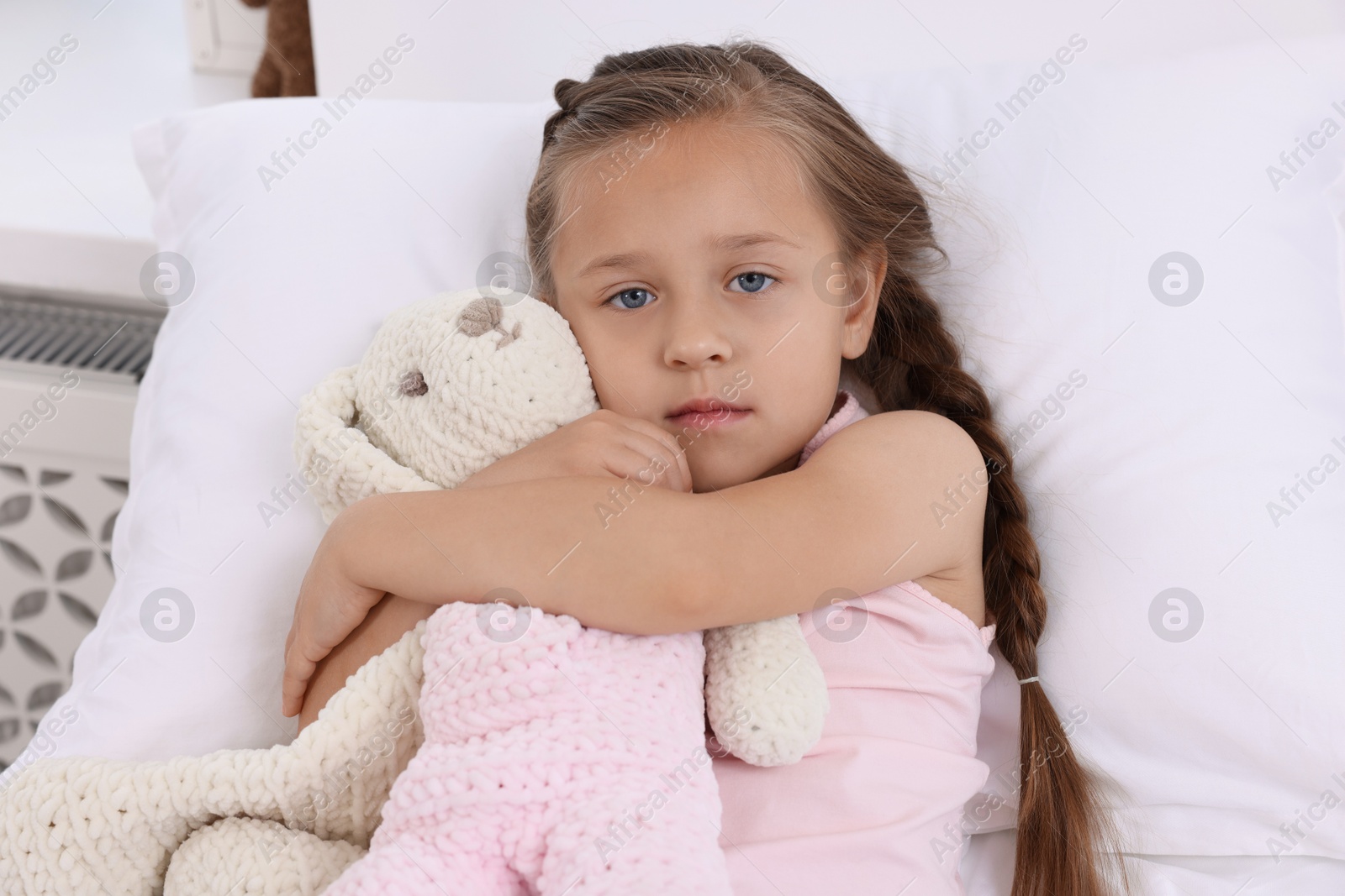 Photo of Cute little girl with toy bunny on bed in hospital