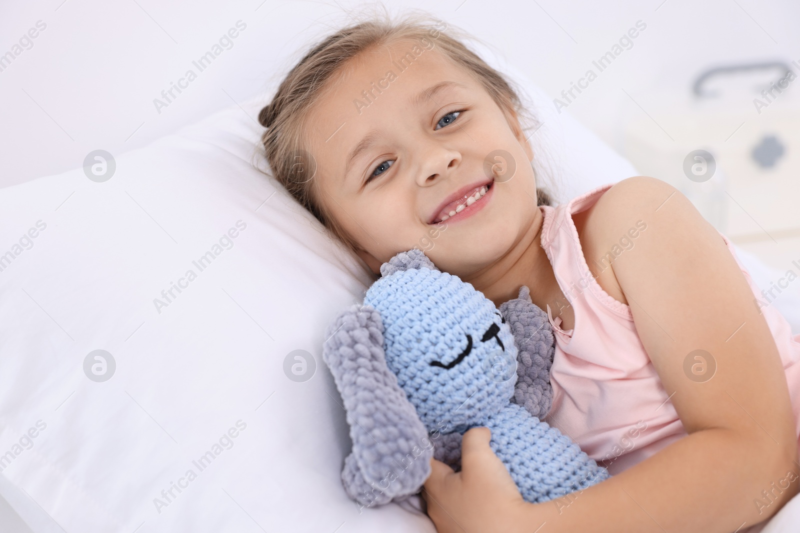 Photo of Cute little girl with toy bunny on bed in hospital