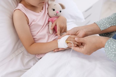 Photo of Mother and her little daughter with IV drip on bed in hospital, closeup