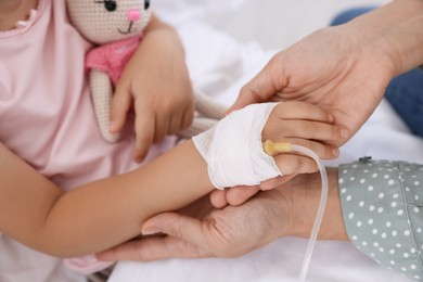 Photo of Mother and her little daughter with IV drip on bed in hospital, closeup