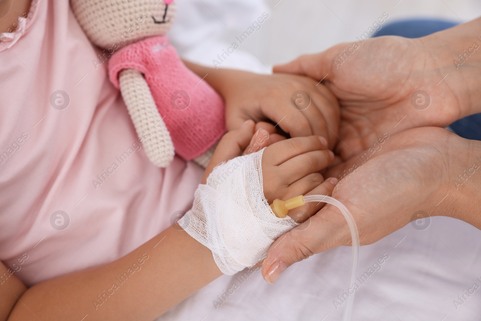 Photo of Mother and her little daughter with IV drip on bed in hospital, closeup