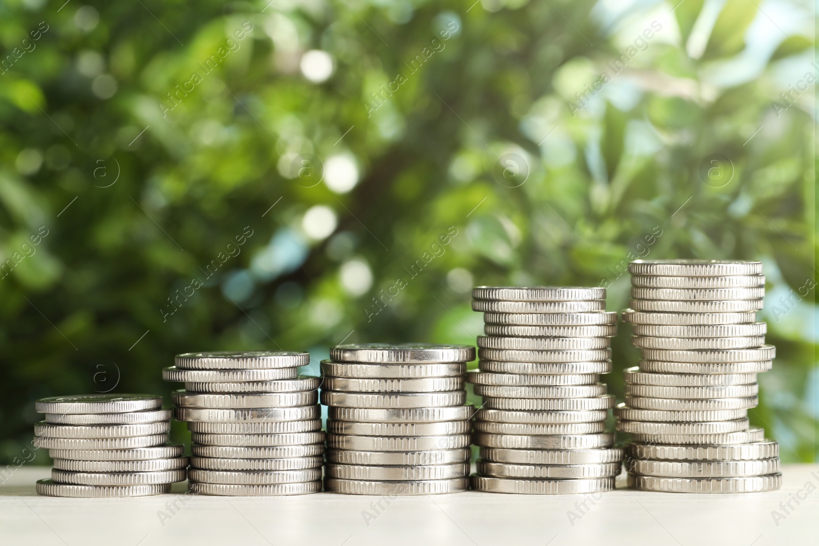 Photo of Stacked coins on white table against blurred green background, closeup. Salary concept