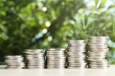 Photo of Stacked coins on white table against blurred green background, closeup. Salary concept