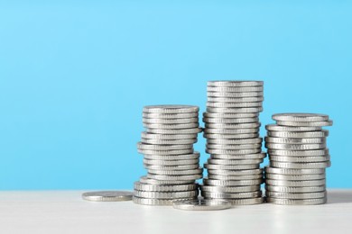 Photo of Stacked coins on white wooden table against light blue background, closeup with space for text. Salary concept