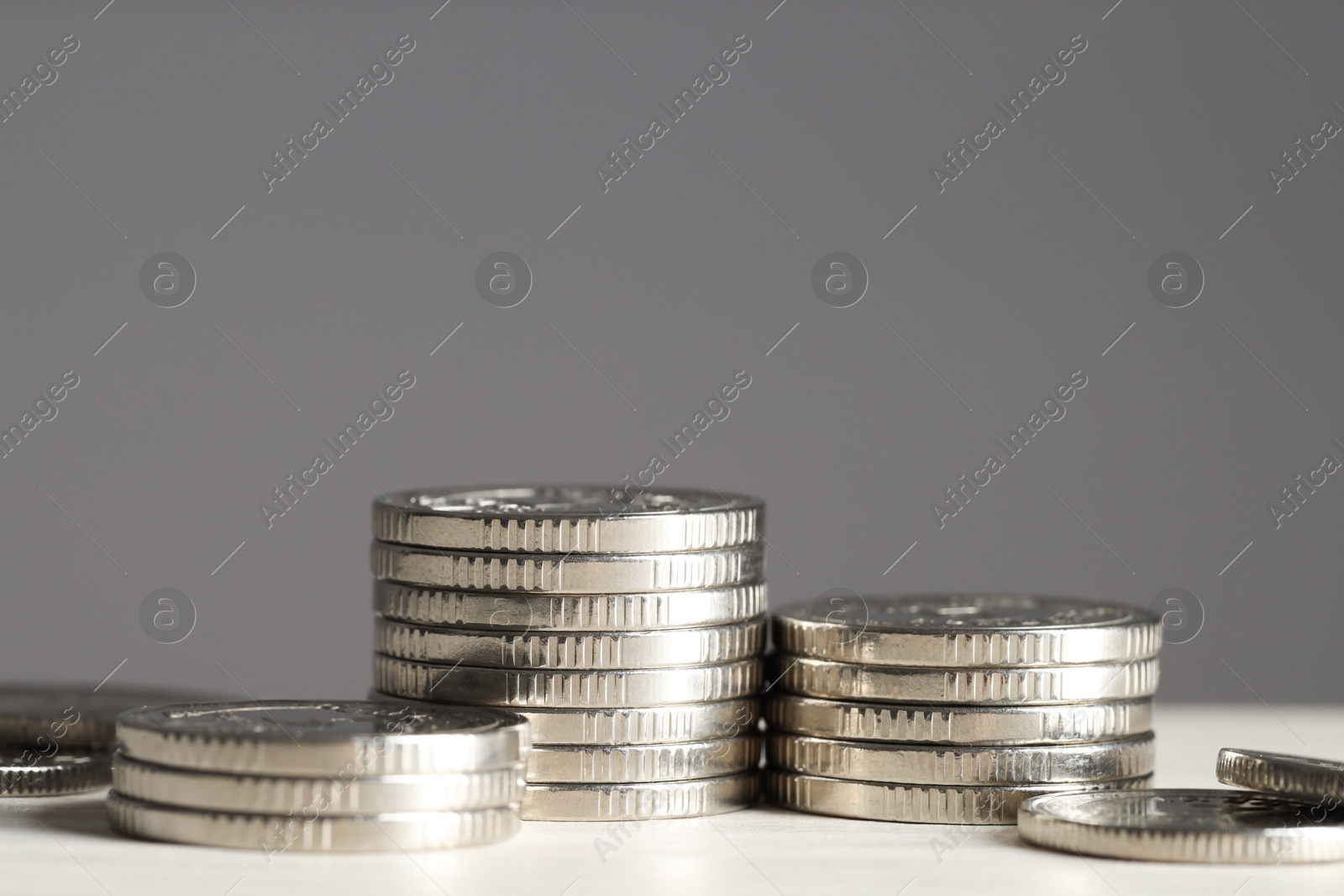 Photo of Stacked coins on white wooden table against grey background, closeup. Salary concept