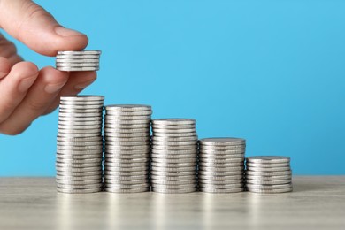 Photo of Woman putting coins at wooden table against light blue background, closeup. Salary concept