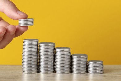 Photo of Woman putting coins at wooden table against yellow background, closeup. Salary concept