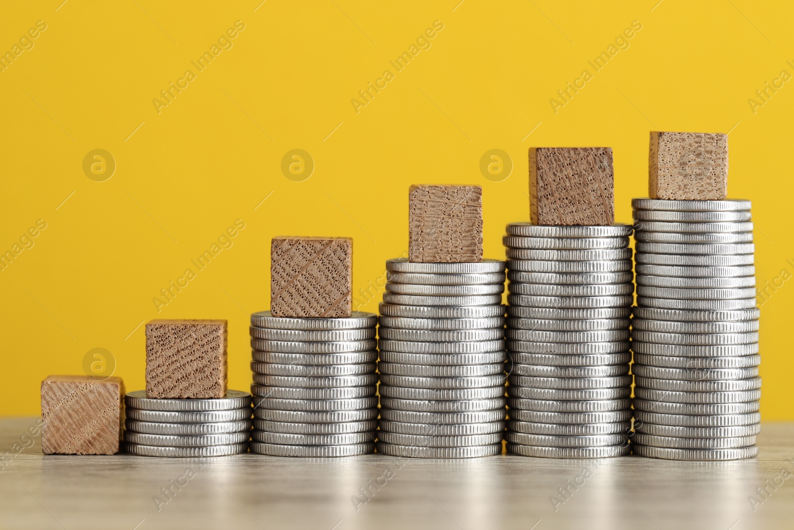 Photo of Blank cubes and stacked coins on wooden table against yellow background, closeup. Salary concept