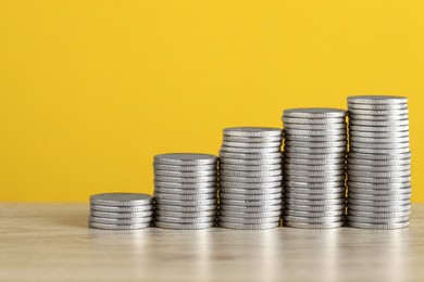 Photo of Stacked coins on wooden table against yellow background, closeup with space for text. Salary concept