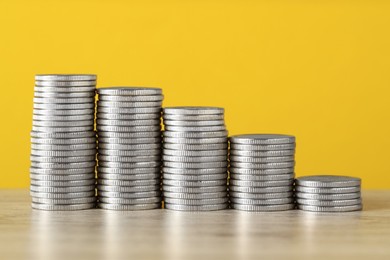 Photo of Stacked coins on wooden table against yellow background, closeup. Salary concept