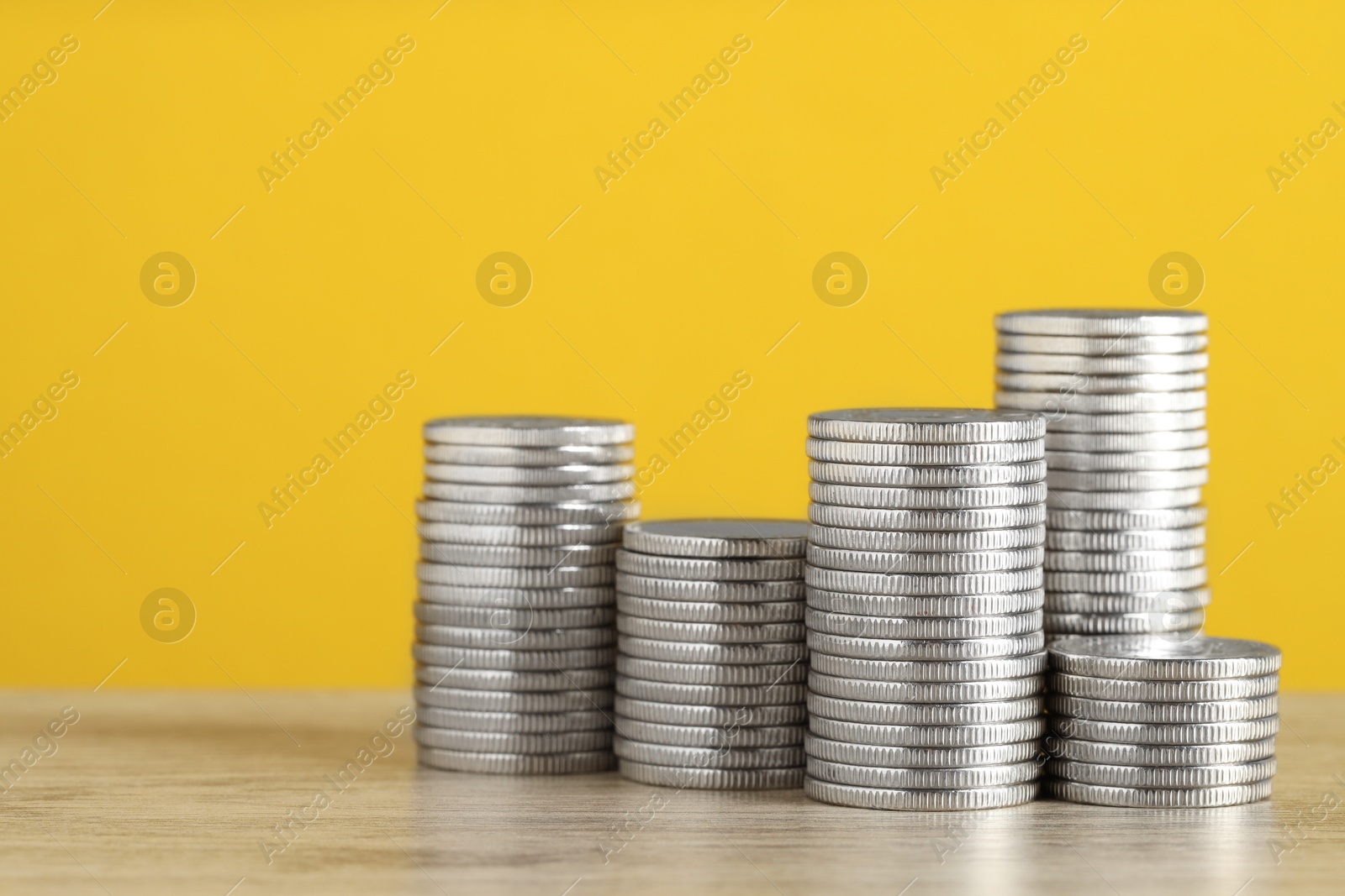 Photo of Stacked coins on wooden table against yellow background, closeup with space for text. Salary concept