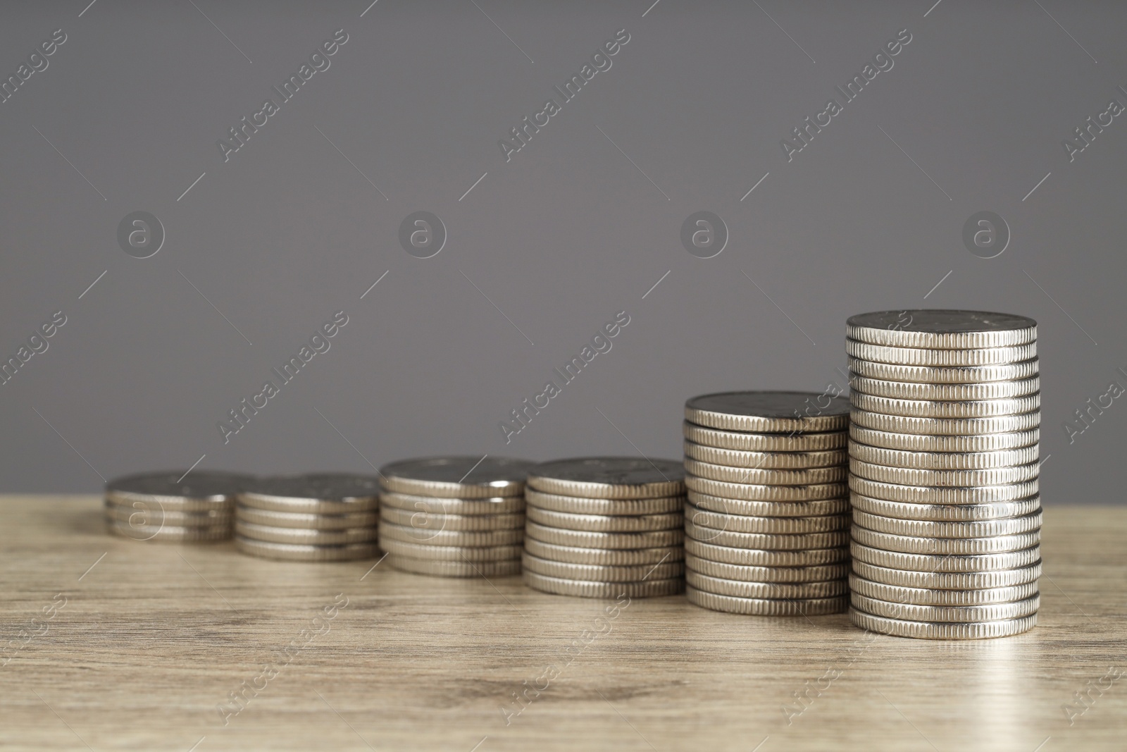 Photo of Stacked coins on wooden table against grey background, closeup with space for text. Salary concept